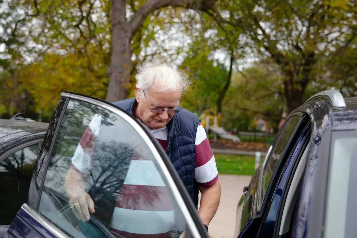 Un homme âgé monte dans une voiture, aidé par le chauffeur